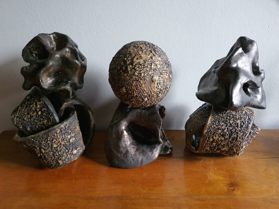 Trzy ceramiczne rzeźby o bogatej fakturze na drewnianym blacie